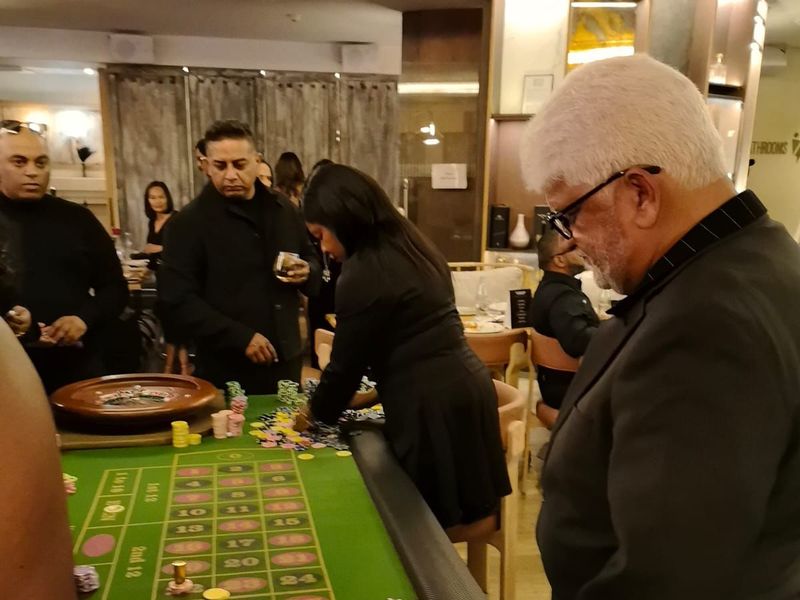 Croupier placing chips on a roulette table as guests in dark evening wear look on