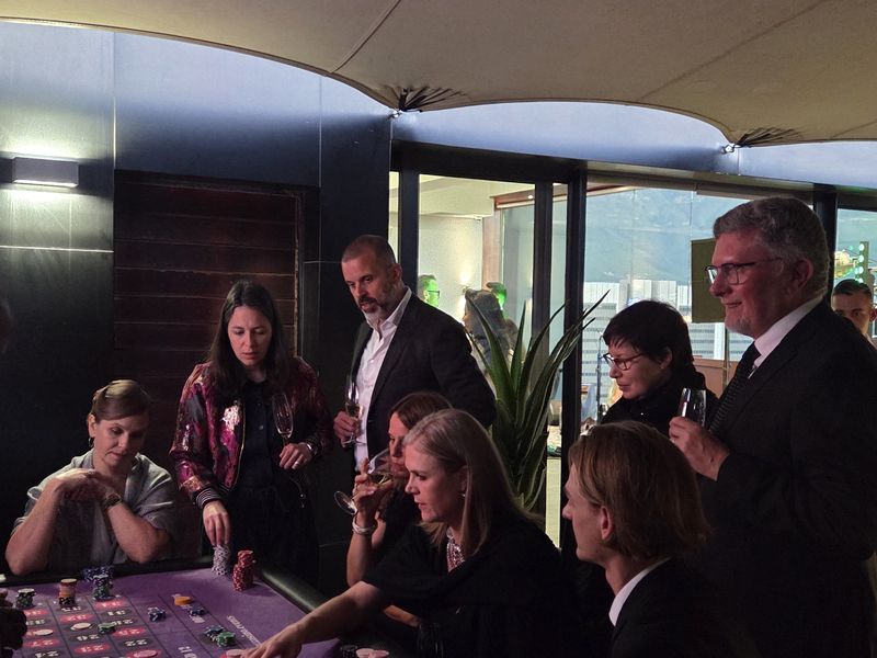 Guests holding champagne around a roulette table at an evening event