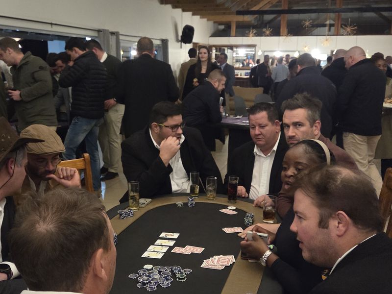 Poker players seated at a busy fun casino night with guests watching