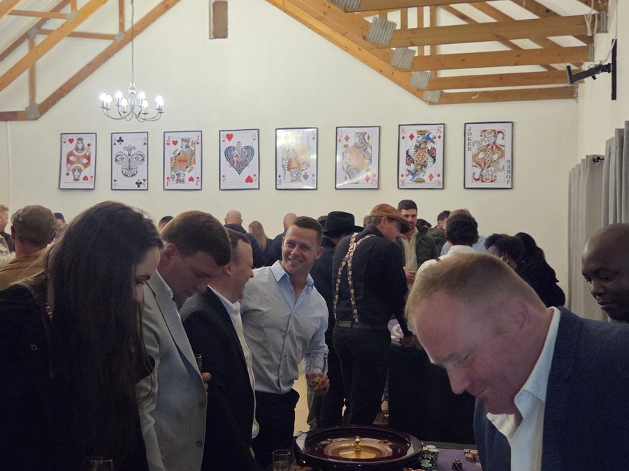 Guests gathered around a roulette wheel at a fun casino night in a hall decorated with playing cards